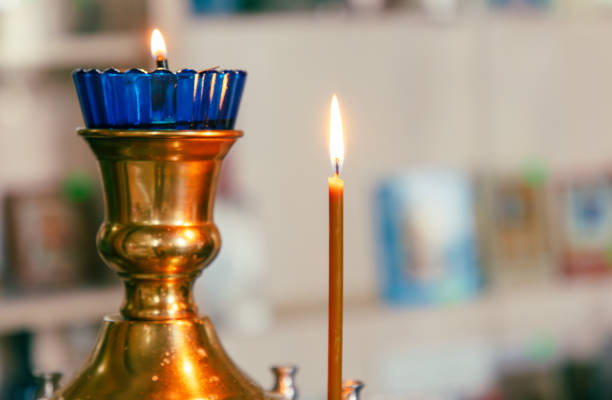 Burning candle in a copper candlestick on a blurred background.