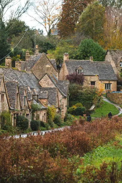 Embrace the Cotswolds' magic with this stunning photo of Arlington Row in Bibury, Gloucestershire. Witness the honey-hued cottages bathed in the warm glow of autumn, their charm accentuated by pockets of vibrant spring blooms. Imagine the tranquil atmosphere as sunlight dances on the crystal-clear stream and reflects on the manicured gardens. This image is a quintessential postcard come to life, offering a glimpse into the pastoral charm of the English countryside.