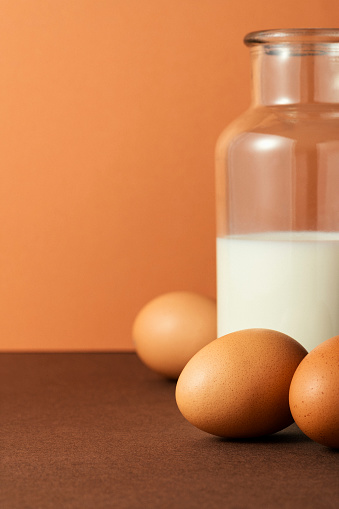 Three eggs with milk in glass bottle on brown background, studio shot with sharp shadows and high contrast