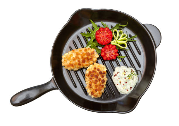 Fried minced meat cutlets with vegetables and sauce on black pan isolated on white background. Chicken Pozharsky cutlets. View from above
