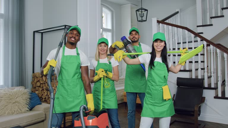 Portrait of multiracial people team man and woman of cleaners in uniforms which posing on camera with cleaning equipment in beautiful apartment