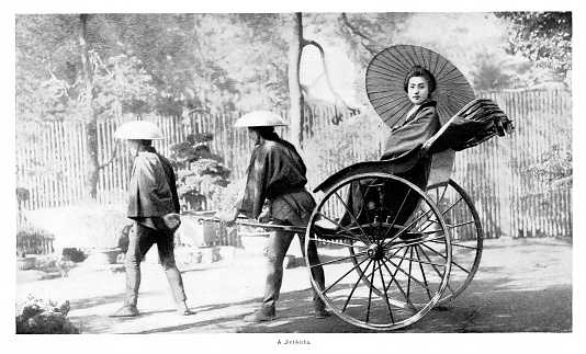 Two Japanese men pull a ricksha,  or jinrikisha, with a  woman riding in the mode of transportation. Engraving published 1894. Original edition is from my own archives. Copyright has expired and is in Public Domain.
