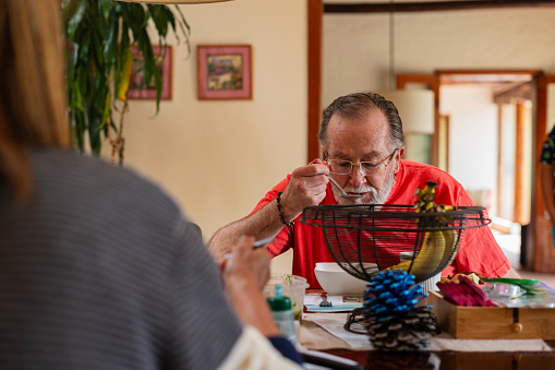 Latino man, approximately 65 years old, dressed comfortably, is inside the gediatric hospital in charge of his care, sitting at the dining room table eating a delicious lunch prepared by his caregivers.