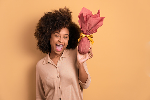 fun black woman with easter egg in beige studio background. holiday, easter, celebration concept.