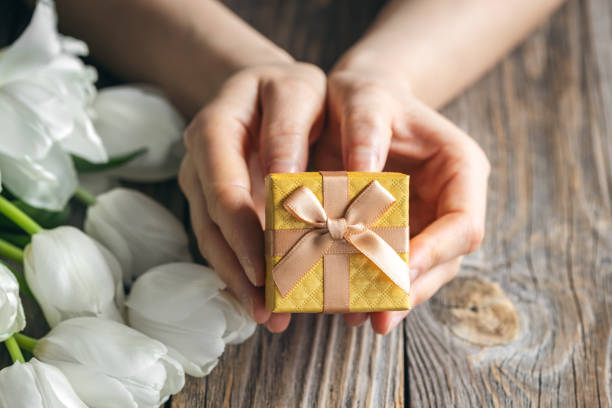 istock Small gift box in female hands on a wooden background with tulips. 2040641828