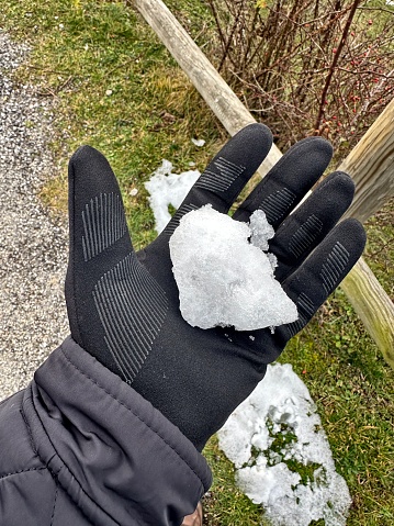 An icy snowball is on a hand wearing a black glove. Snow-covered grass can be seen in the background.
