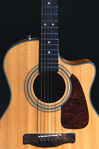 Acoustic guitar on a black background, flat lay. Acoustic guitar made of wood with cutaway close up on dark background.