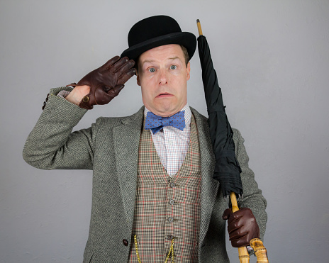 Man in Tweed Suit and Bowler Hat Saluting While Holding Umbrella Like a Rifle