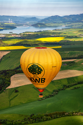 Liptovsky Mikulas, Slovakia - Jun 2, 2021: Yellow hot-air balloon and beautiful green fields and lake Liptovska Mara under in Liptov area