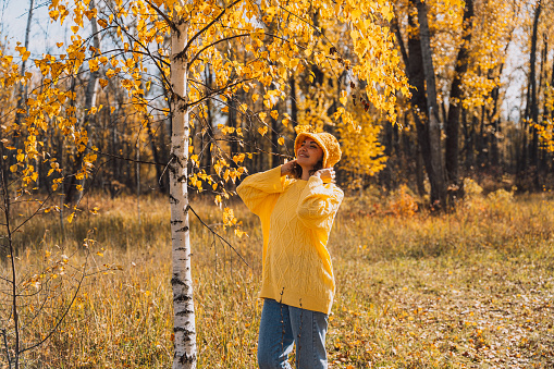 A lady in a yellow knitted sweater walks through the autumn forest.