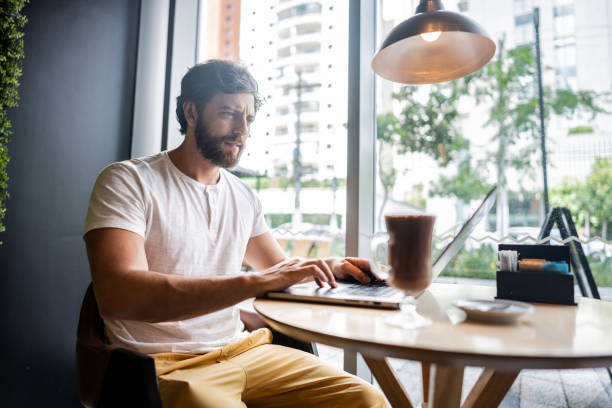 istock Mid adult man using laptop to work at coffee shop 2040707611
