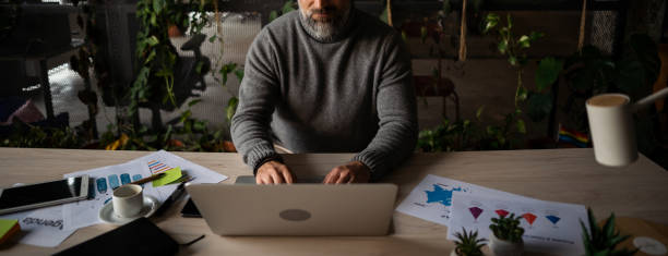 istock A man in a sitting position at a wooden table, using a laptop computer 2040708184