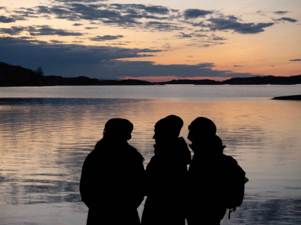 silhouette di quattro persone sulla spiaggia al tramonto con il sole al tramonto - silhouette three people beach horizon foto e immagini stock