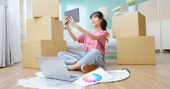 Asian woman happy sit floor hold tablet look at interior design - hand gesticulating in air she imagine decoration of her new home