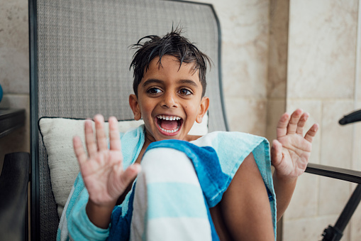 Close up shot of boy showing his wrinkled hands from the swimming pool in Northumberland. His hair is wet and he is wrapped up in a blue swim towel and resting on a lounge chair after being in the swimming pool. Focus on boys face.