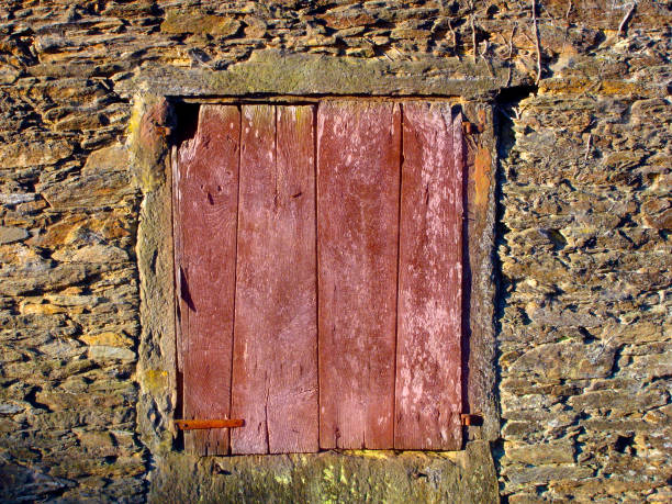Part of old weathered stone facade and closed window with red shutter. Galicia, Spain.