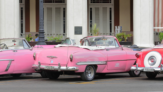 Havana, Cuba-October 07, 2019: Three pink-red classic American convertible cars -almendron, yank tank- Mercury Monterey 1953-Chevrolet Bel Air 1953-Ford Crestline Victoria 1953 park on Paseo del Prado