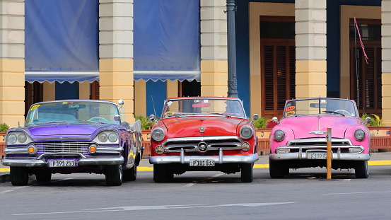 Havana, Cuba-October 07, 2019: American classic convertible cars, purplish blue Dodge Custom Royal Lancer 57-red Ford Crestline Sunliner 52-pink Chevrolet Styleline DeLuxe 52 park on Paseo del Prado.