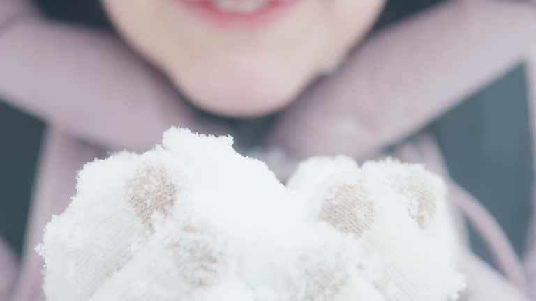 Winter caucasian girl in the hood blowing on the snow in her hands.