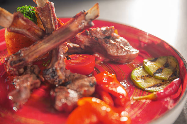 nahaufnahme eines gegrillten lammkoteletts mit geröstetem gemüse auf einem roten teller - animal bone chop close up color image stock-fotos und bilder