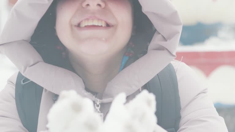 Winter caucasian girl in the hood blowing on the snow in her hands.