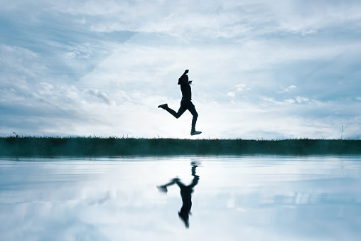 man jumping in the field and reflecting in the lake