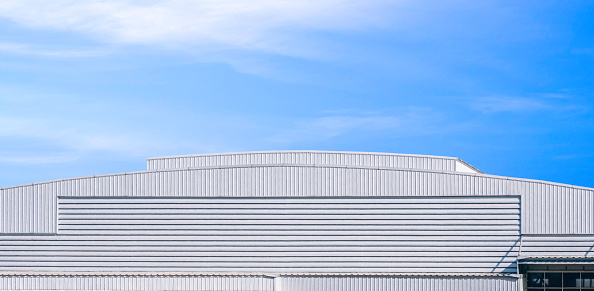 Large white aluminum industrial factory building with dome roof in modern style against blue sky background in panoramic view