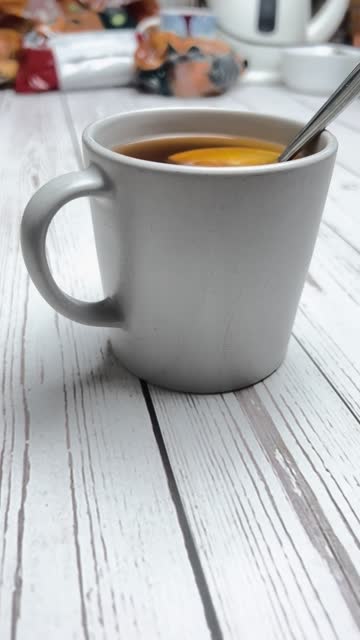 Stir in tea with two slices of ripe lemon with a spoon and cool in a gray cup on a white wooden table. Side view.