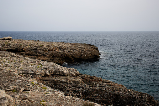 typical coast line with dark blue sea and jagged rocks with few green plants in Menorca