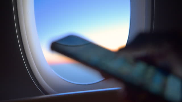 Close up of a man looking at a mobile phone with an airplane window in the background.