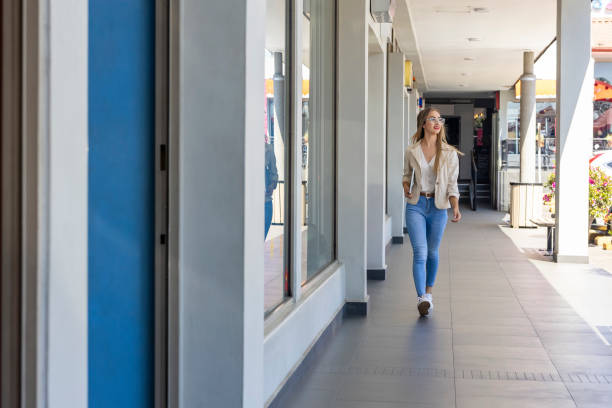 blurred silhouette of a person with a backpack walking away down a wide corridor toward a brightly lit, modern retail store entrance in a shopping mall