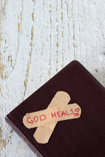 God heals, handwritten text on bandage placed on closed holy bible book. Top view. Christian biblical concept of grace, love, repentance, forgiveness, compassion, and mercy.