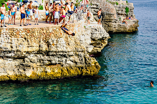 Cala En Brut, Menorca, Balearic Islands, Spain; July 8, 2023: People jumping from rocks into the sea in summer