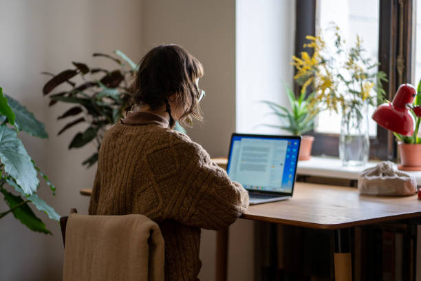 Focused concentrated woman freelancer working on laptop reading documents sitting at desk at home.