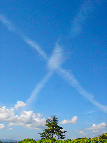 Airplane trails of condensed air crisscrossing each other, blue sky background. X letter. Galicia, Spain.