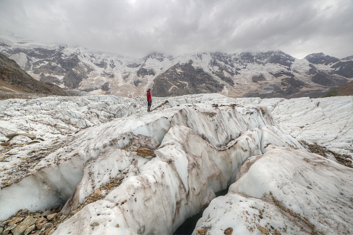 A small figurine of a man stands on the glacier. There are high mountains in the background.