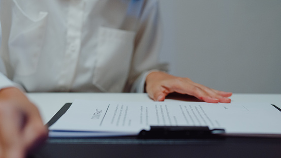 Closeup of young Asian businessman mentor corporate leader manager counselor communicate with businesswoman and sign a contract at office night. Businesspeople in workplace concept.