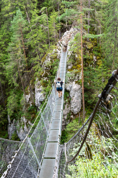 istock Woman with backpack walking on suspension bridge in mountains 2040874028