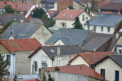 Peaceful and family-friendly view of a residential area of detached houses, typical of the 1970s suburban housing estates, in Maisons-Alfort. Orange tiled roofs dotted with chimney flues and Velux windows, a few red brick facades and tree-lined gardens.