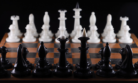 Close-up. Black chess pieces opposite white ones, along the board. On isolated black background