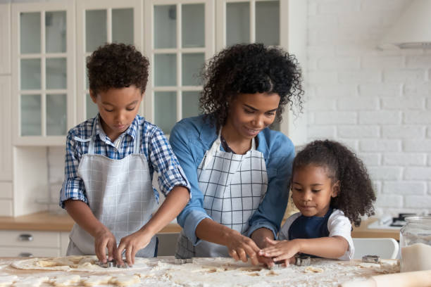 Happy African American mother teaching kids making cookies.