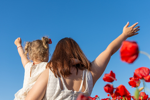 Mother with daughter in her arms near red poppy flowers