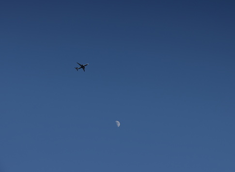 A passenger airplane flies over Metro Vancouver. Background shows the moon and clear sky in winter.