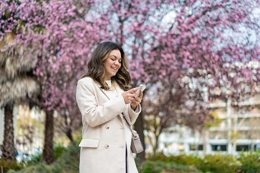 Mature woman using smartphone under flowering tree in spring