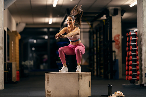 A fit woman is jumping on a box in a gym with heart rate belt.