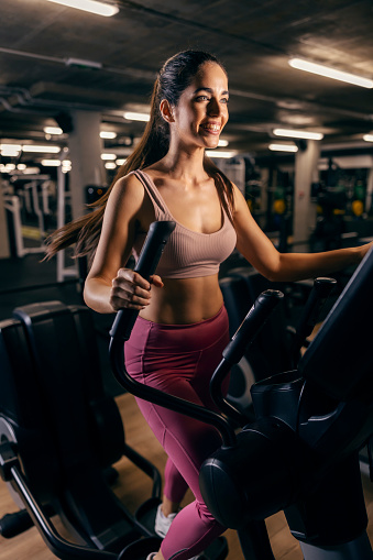 A happy fit woman doing workouts on ski machine in a gym.