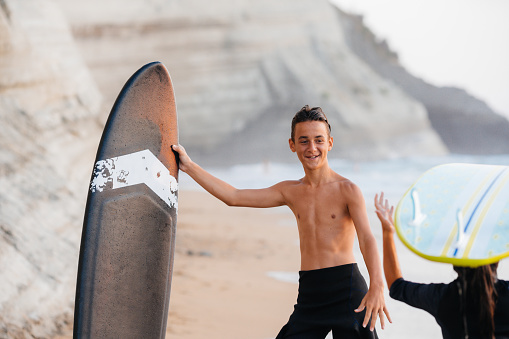 Teenagers smiling and talking on the beach, holding their surfboards and prepare to enter in to the waves