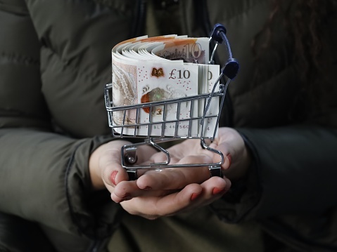 hand of a woman holding a shopping cart and pound sterling notes