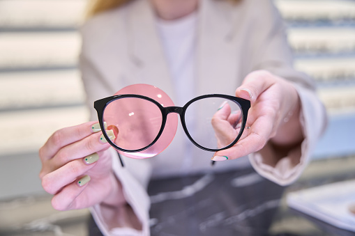 Woman holds glasses and an ophthalmic gadget in her hands, a specialist at his workplace in an optics salon
