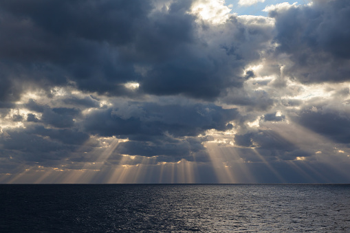 The sun's rays make their way through the cloudy sky overcast in the open sea.